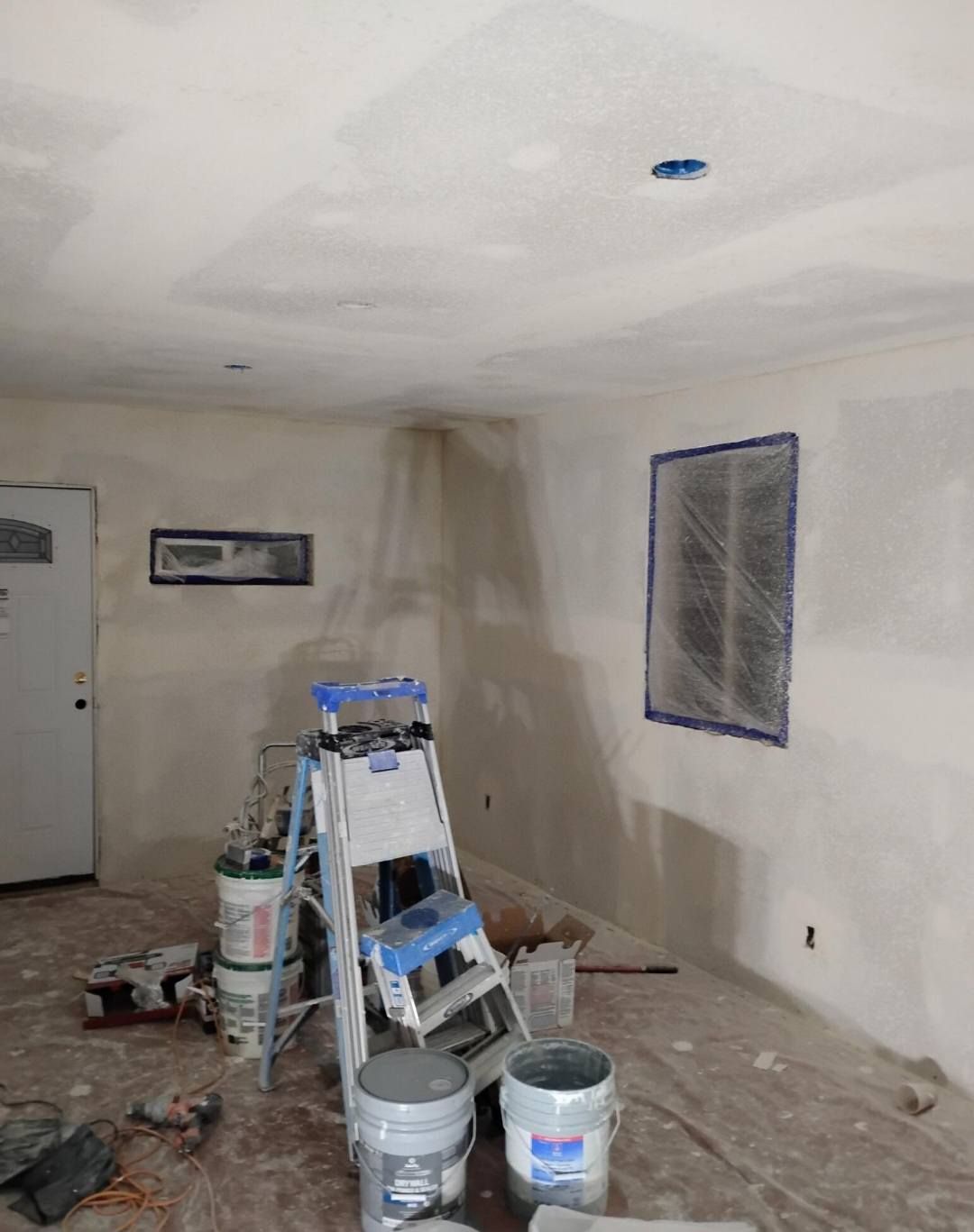Room under renovation, ladder, buckets, taping, and drywall work.