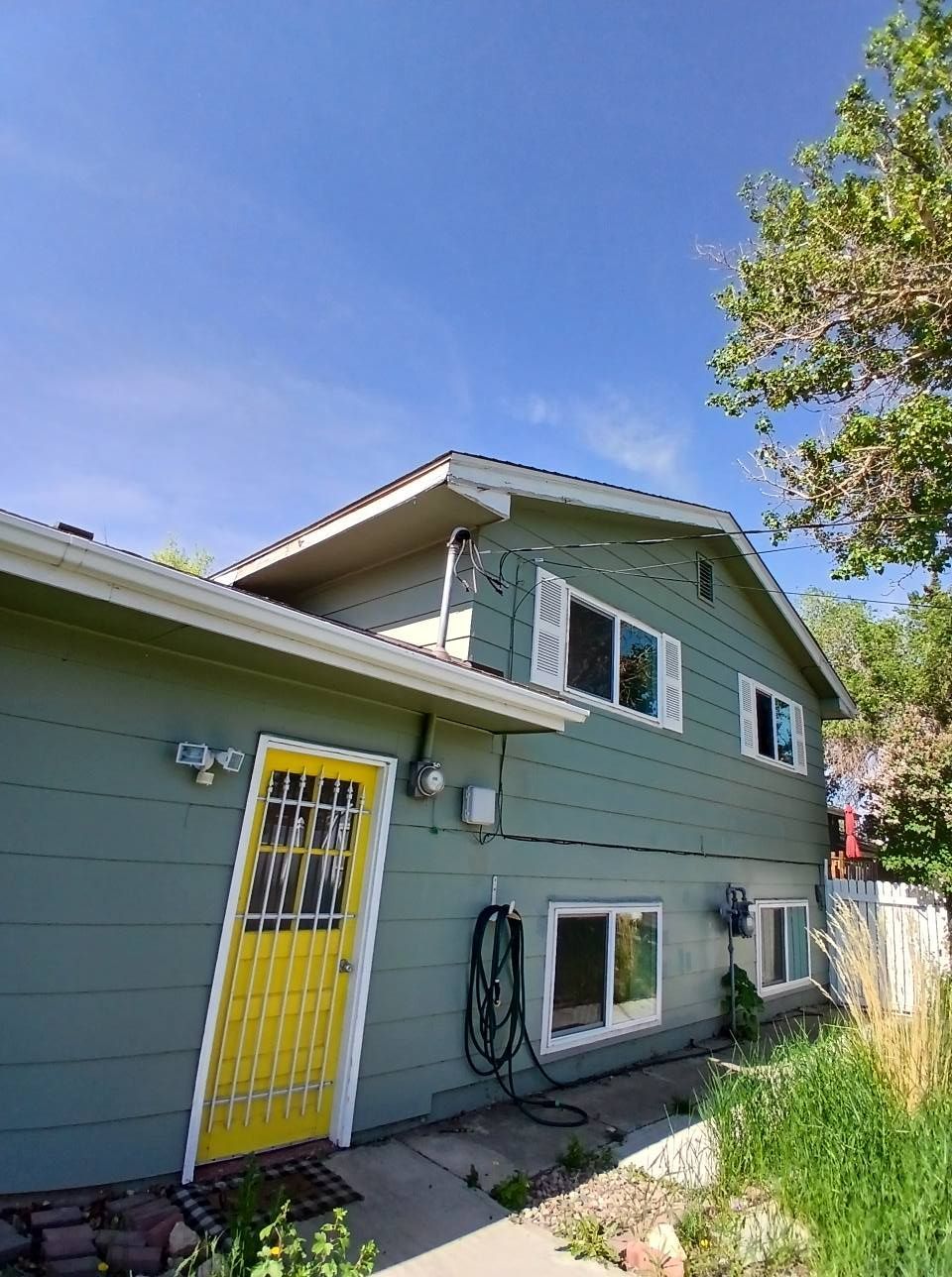 Two-story house with green siding, yellow door, white shutters, and blue sky.