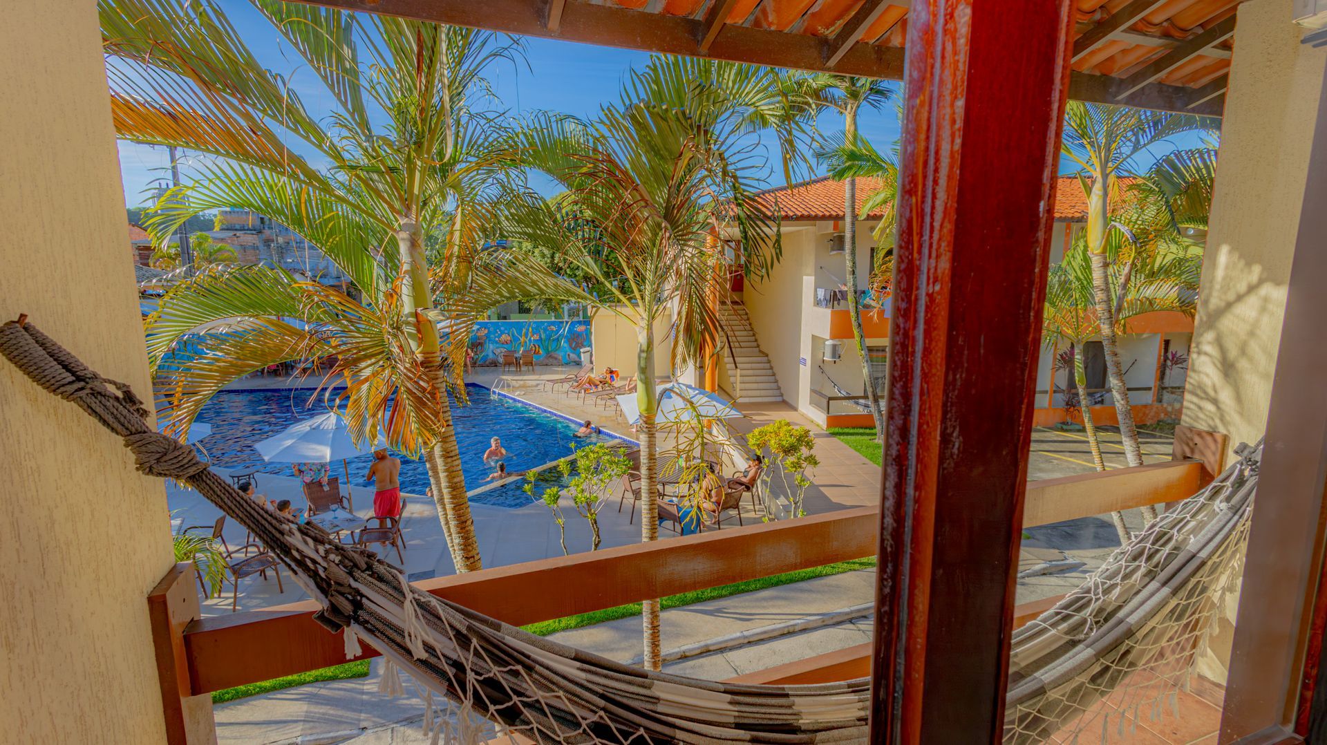 Vista da piscina e do ambiente tropical a partir de uma varanda com rede.