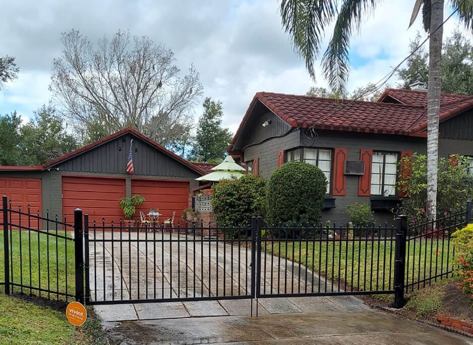 A black fence surrounds a driveway in front of a house.