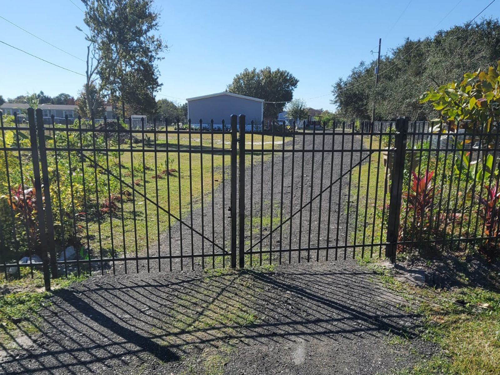A black wrought iron gate is open to a gravel driveway.