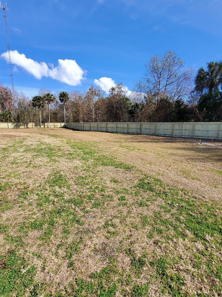 A large empty field with a fence and trees in the background.