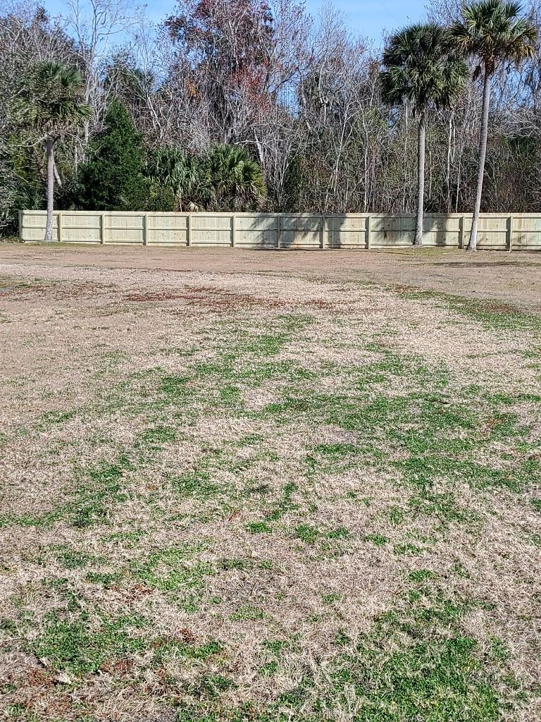 A large empty field with a fence and trees in the background.