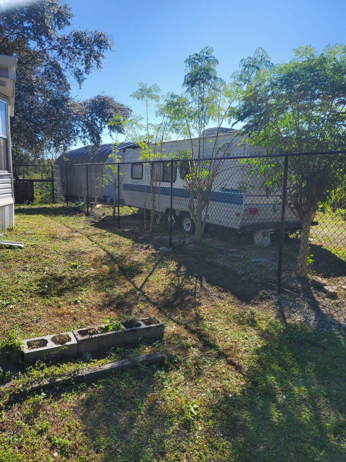 A trailer is parked behind a chain link fence next to a house.