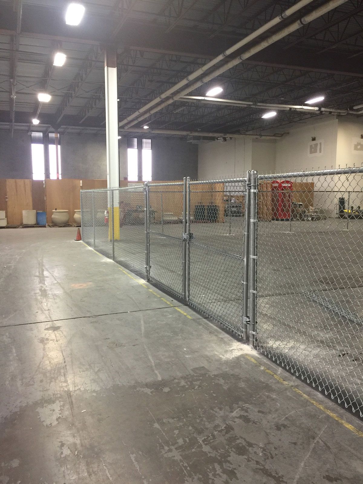 There is a chain link fence in the middle of a large warehouse.