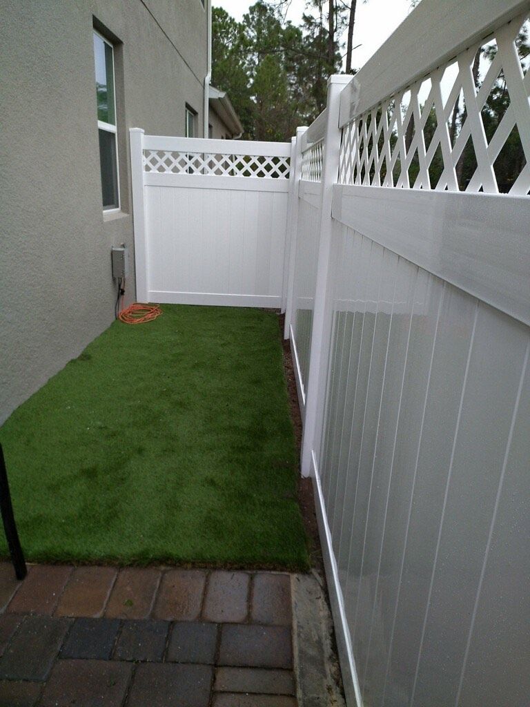 A white fence surrounds a grassy area in front of a house.