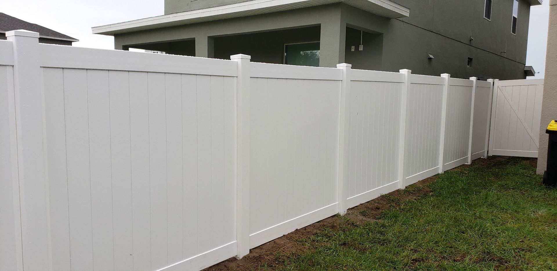 A white fence is in the backyard of a house.