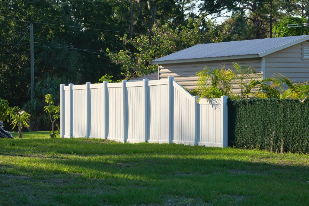 A white fence surrounds a lush green yard in front of a house.