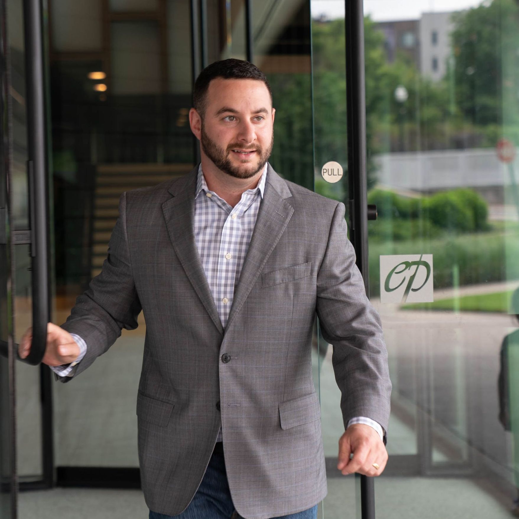 A man in a suit is standing in front of a glass door.