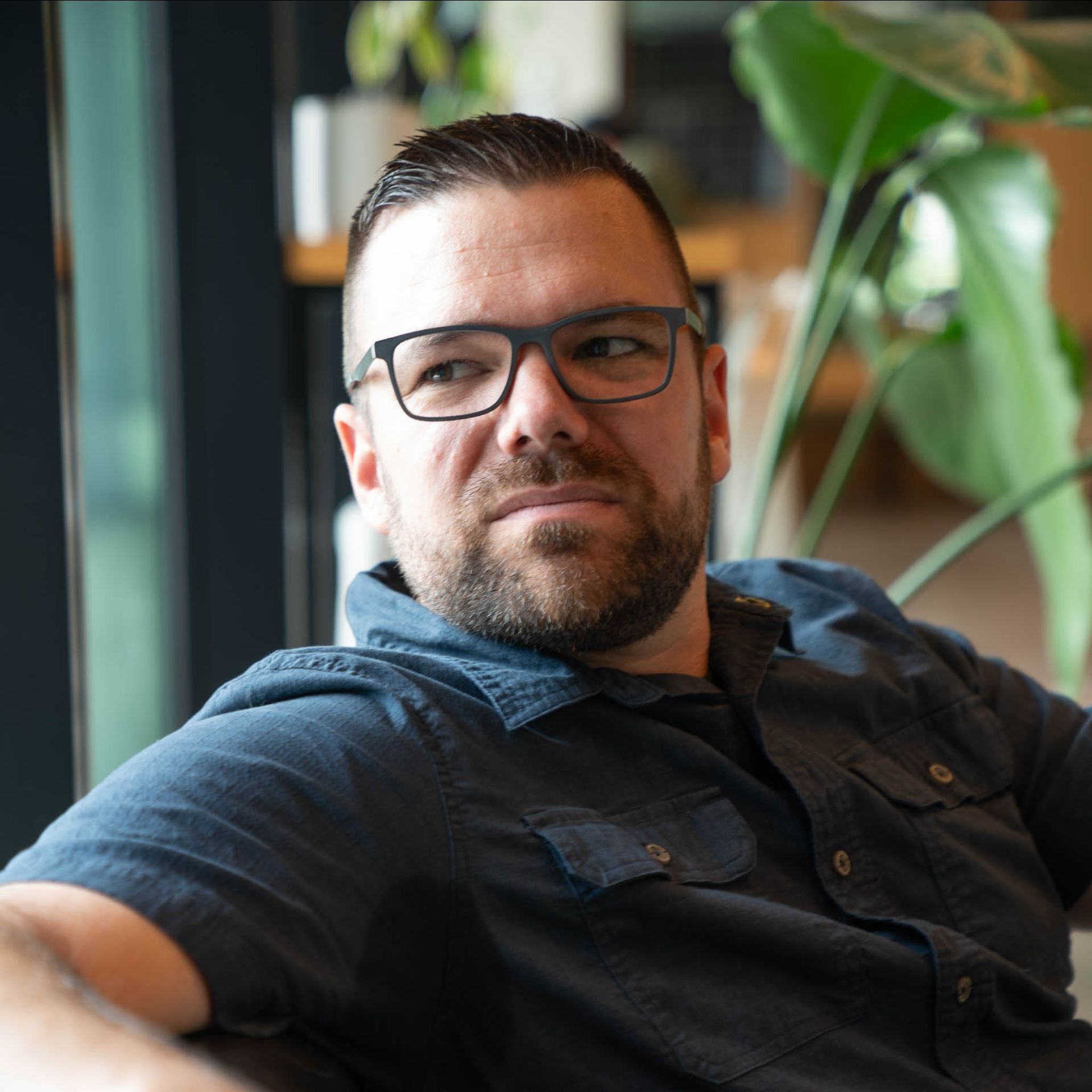 A man with a beard and glasses is sitting on a couch.