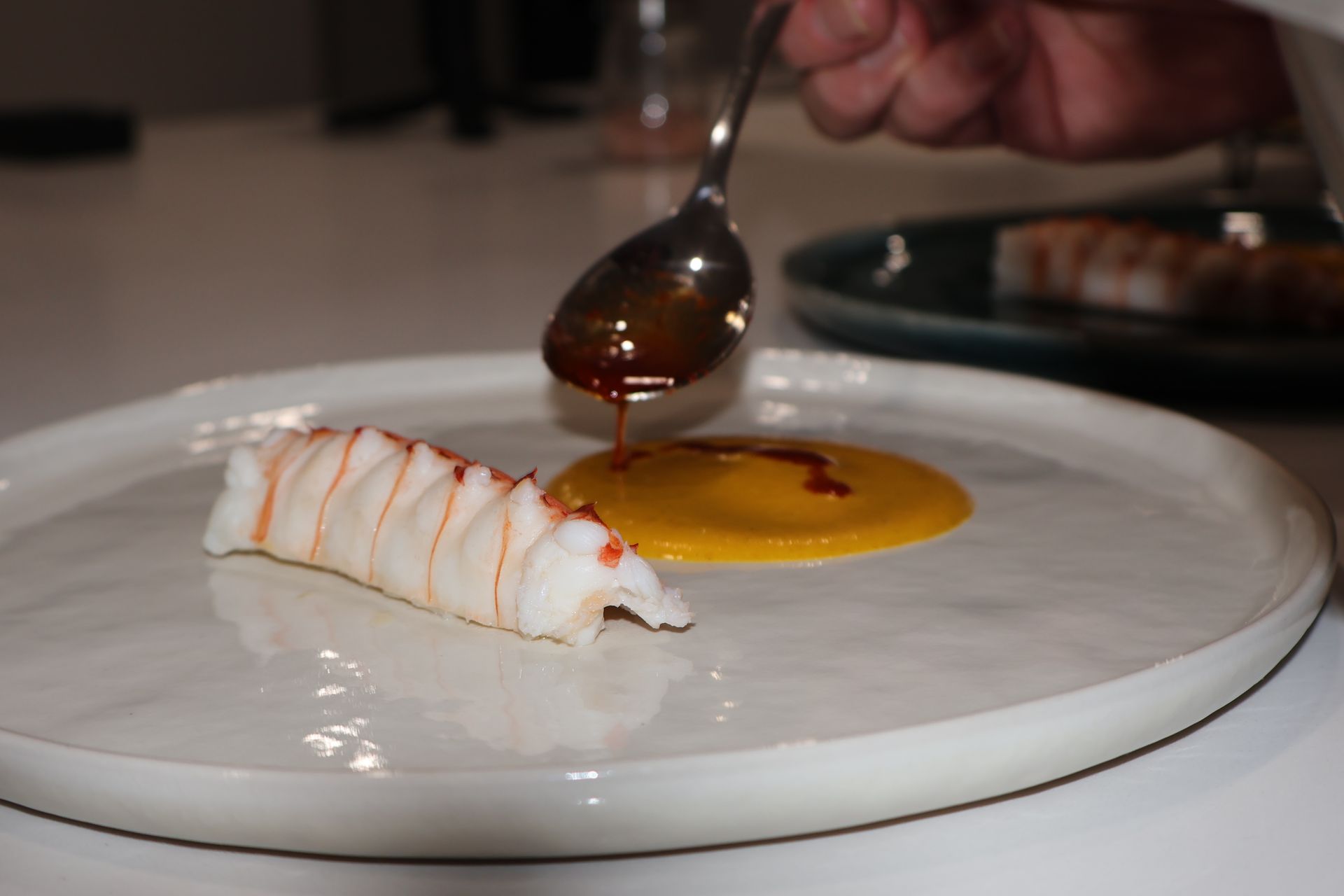 A chef plating a lobster tail with sauce on a white plate.