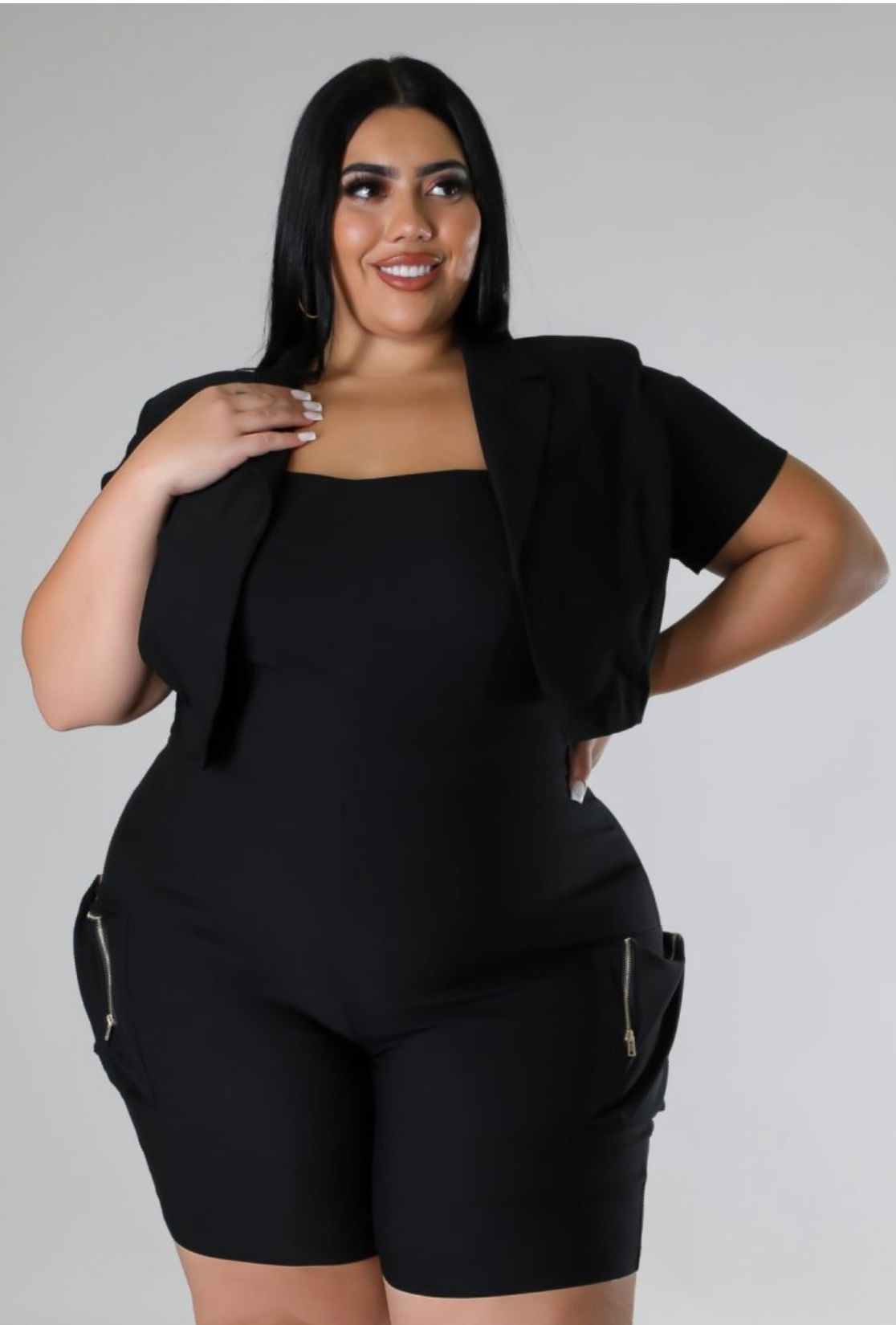 A plus size woman is wearing a black jumpsuit and shorts.