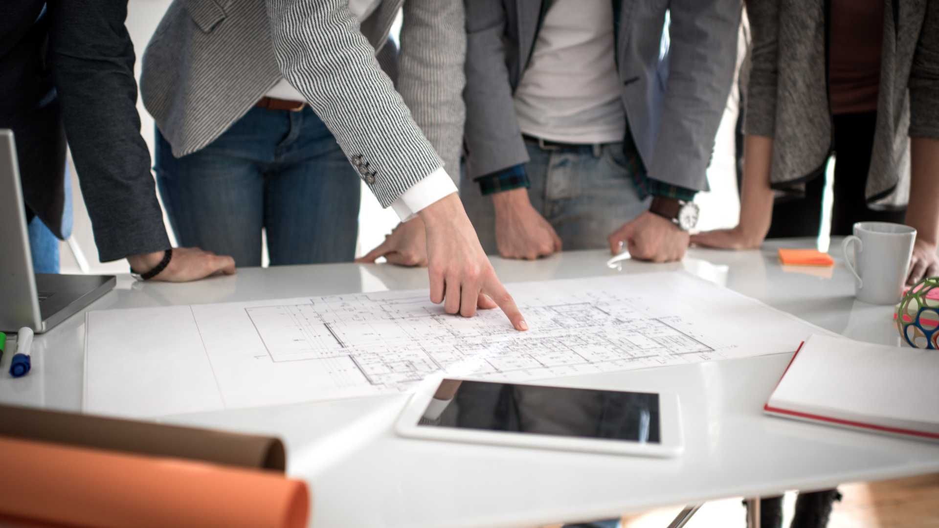 A group of people are standing around a table looking at a blueprint.