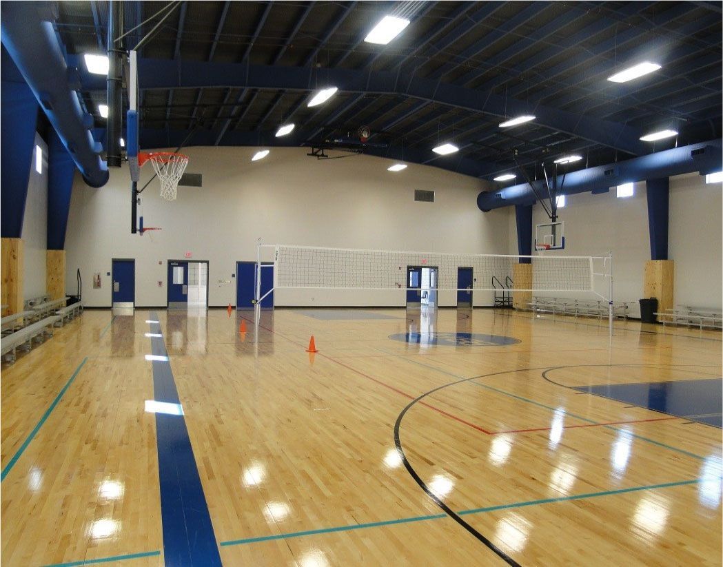 An empty gym with a volleyball net and a basketball hoop