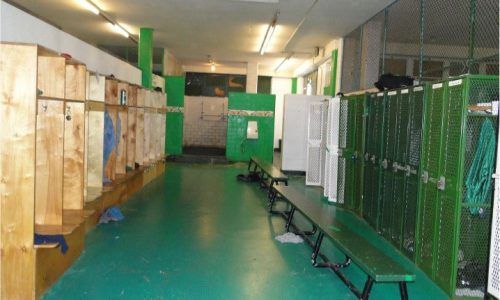 A locker room with lots of green lockers and benches