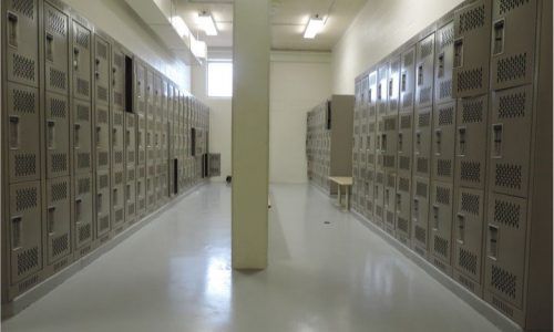 A long hallway filled with lots of lockers and a bench.