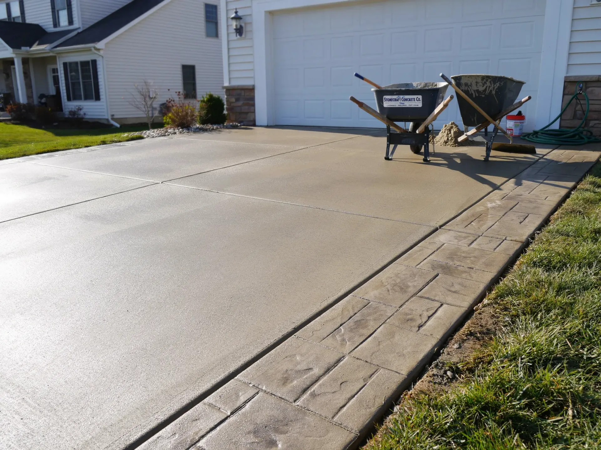 Freshly poured concrete driveway beside a house with two wheelbarrows near the garage.