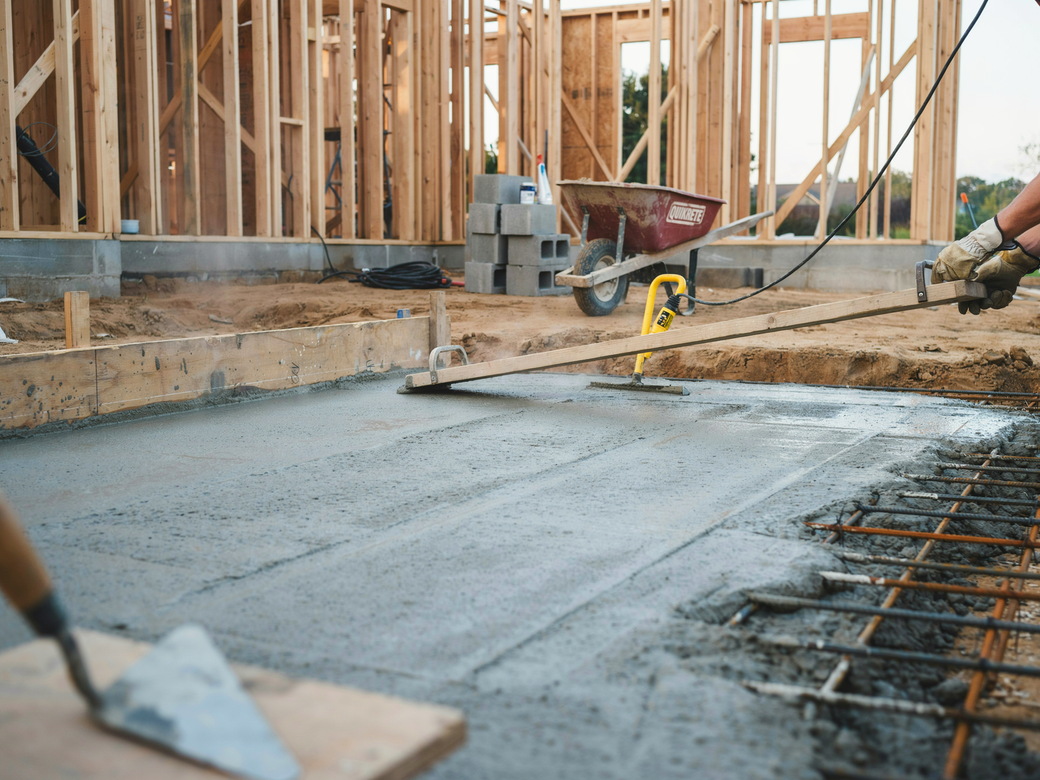 Wet concrete being poured at a house foundation during construction, with tools and rebar visible.