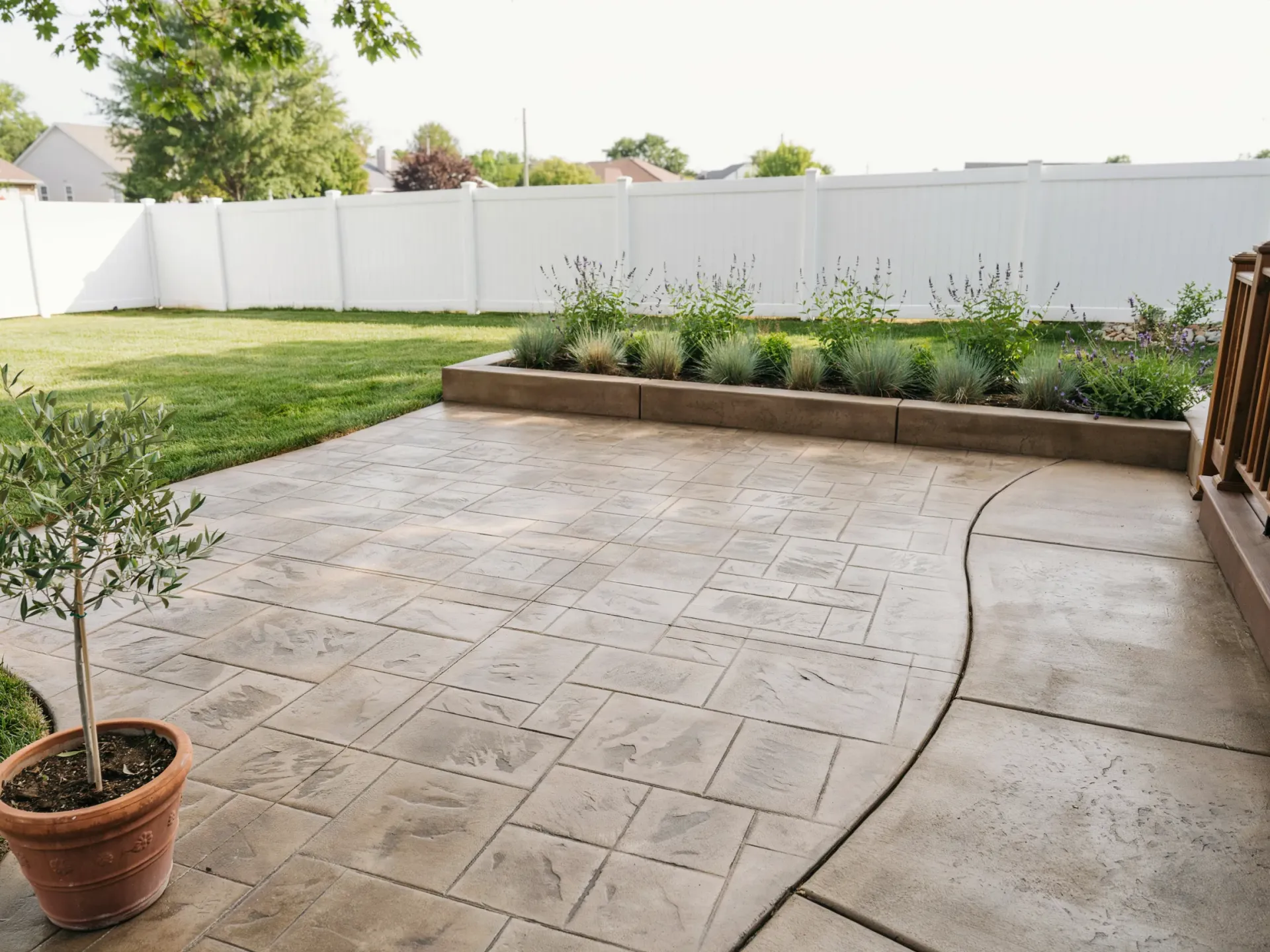 Patio with stamped concrete, potted tree, raised planter bed, lawn, and white privacy fence