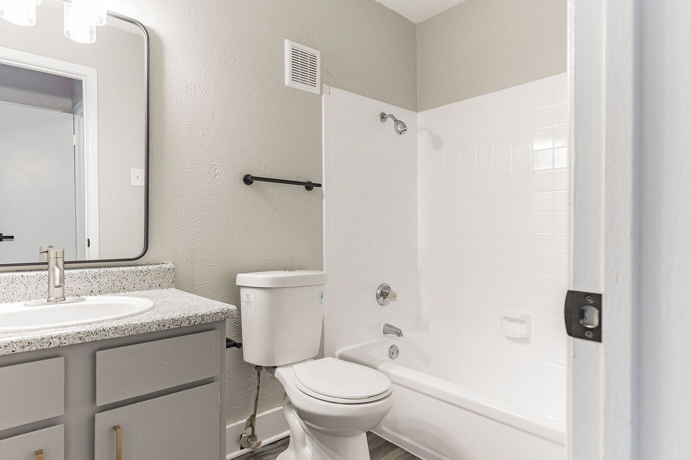 Bathroom with white tub and toilet, gray vanity, and textured gray walls.