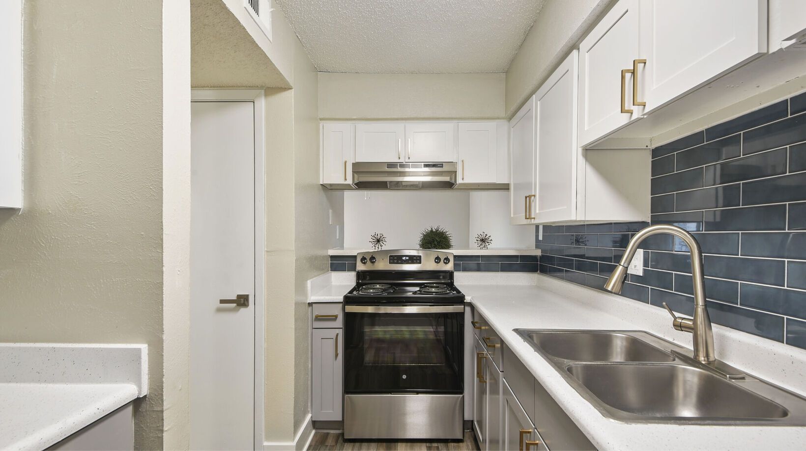 White kitchen with stainless steel appliances, blue backsplash, and white countertops.