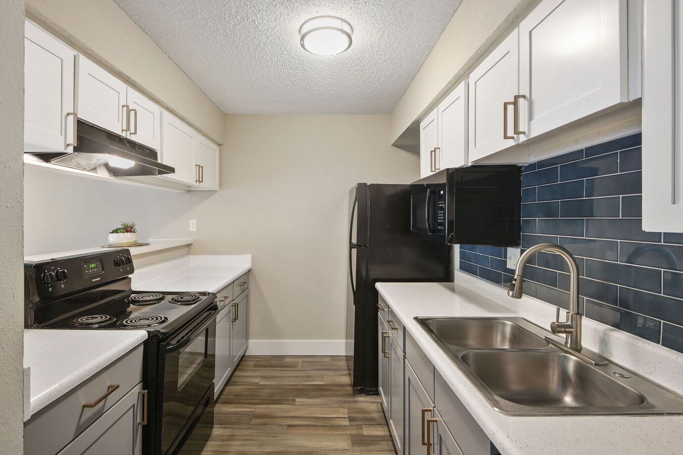 Narrow galley kitchen with white cabinets, gray lowers, black appliances, and blue tile backsplash.