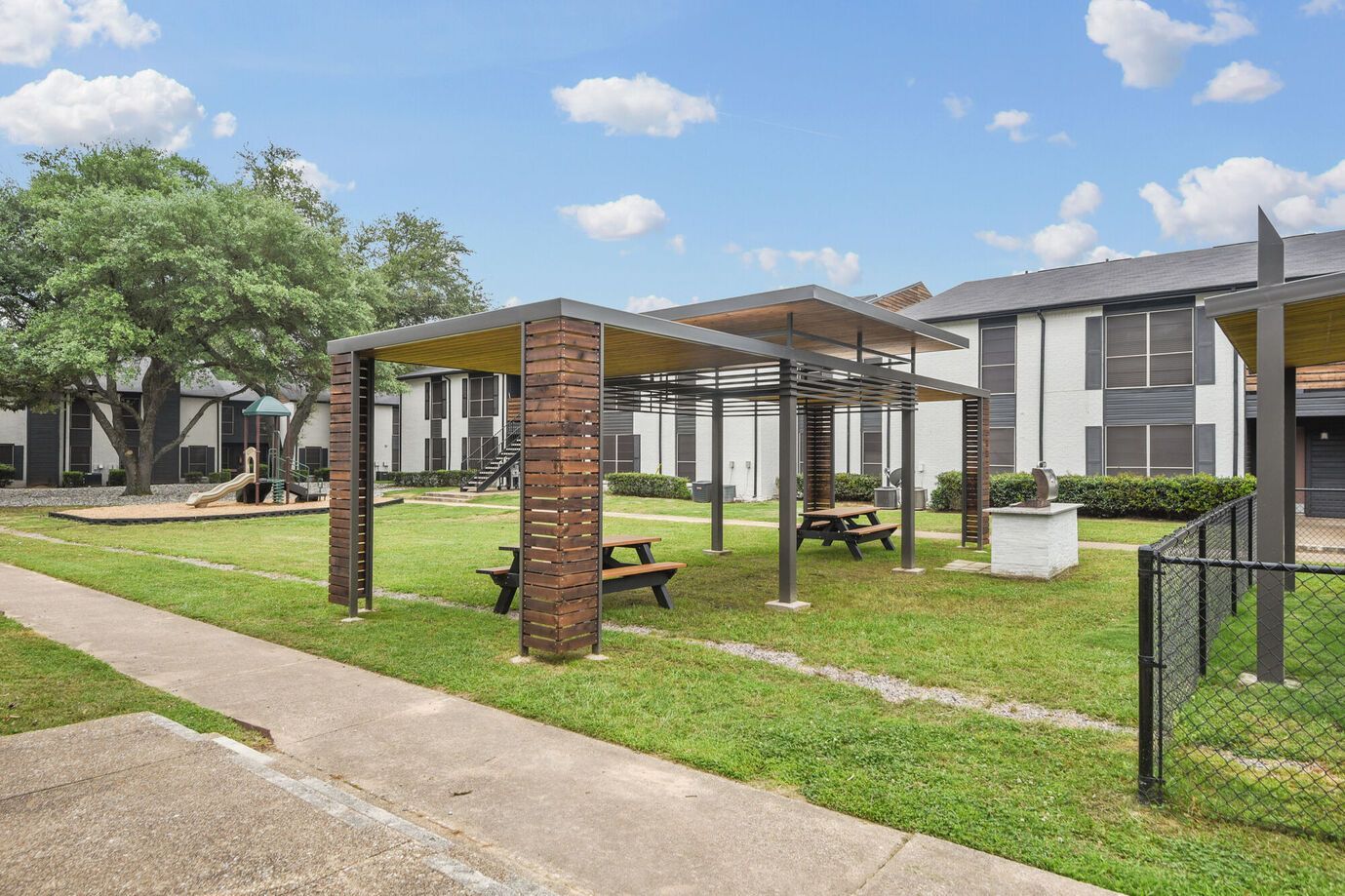 Park area with a gazebo, picnic tables, and apartment buildings in the background.