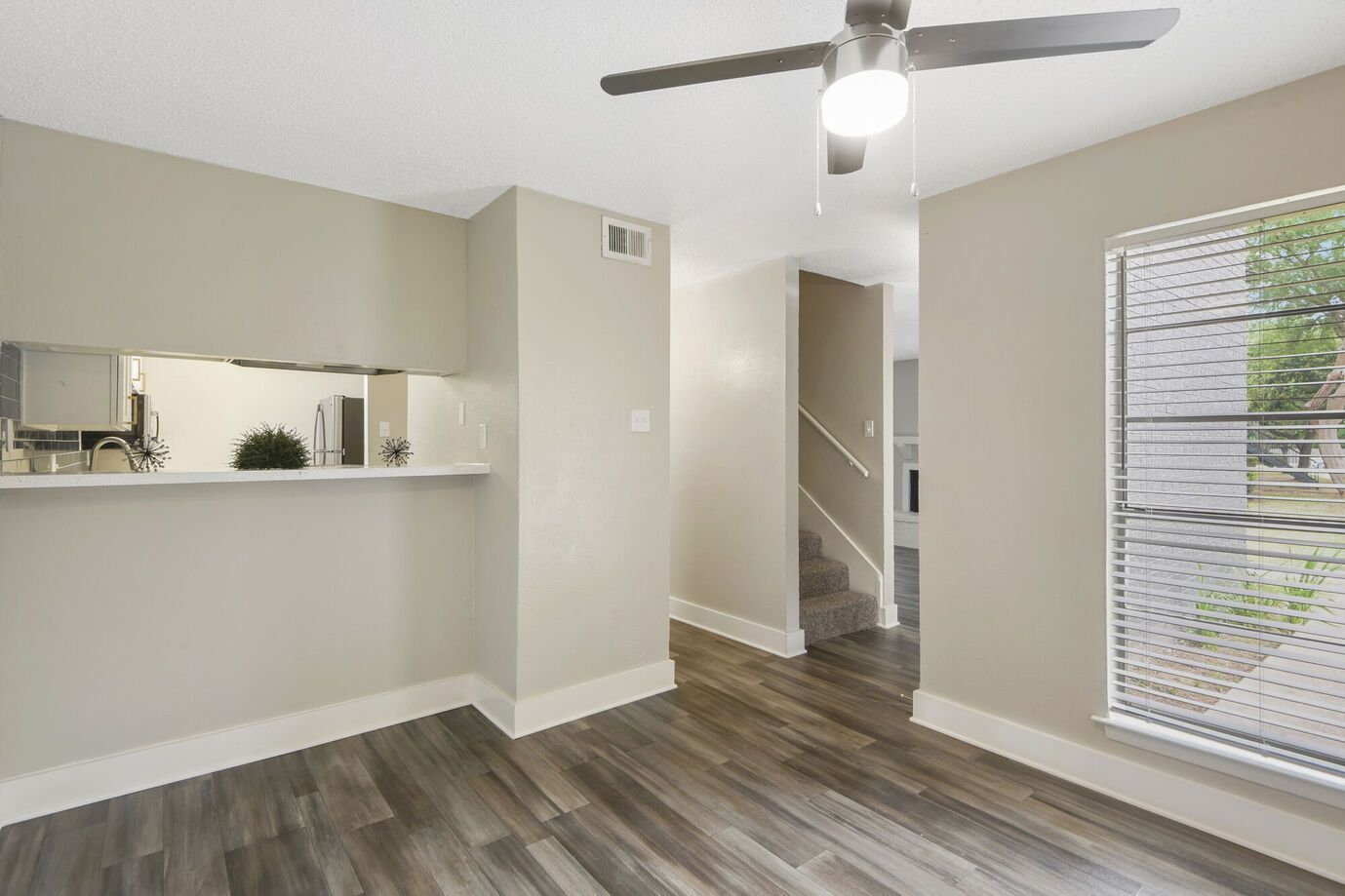An empty room with gray walls, dark wood-look floor, a window, and a ceiling fan.