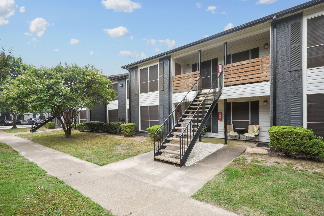 Apartment building with stairs, gray siding, wooden balconies, and green grass.