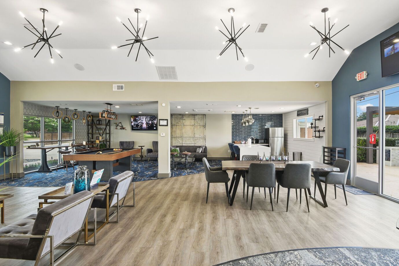 Lounge area with tables, chairs, fireplace, and pool table. Light wood floors, neutral walls, and sputnik-style lights.