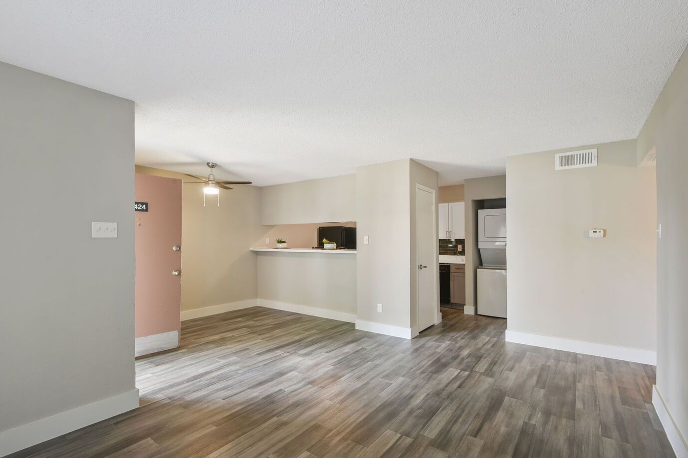 Empty apartment interior with wood-look floors, light gray walls, and a small kitchen.