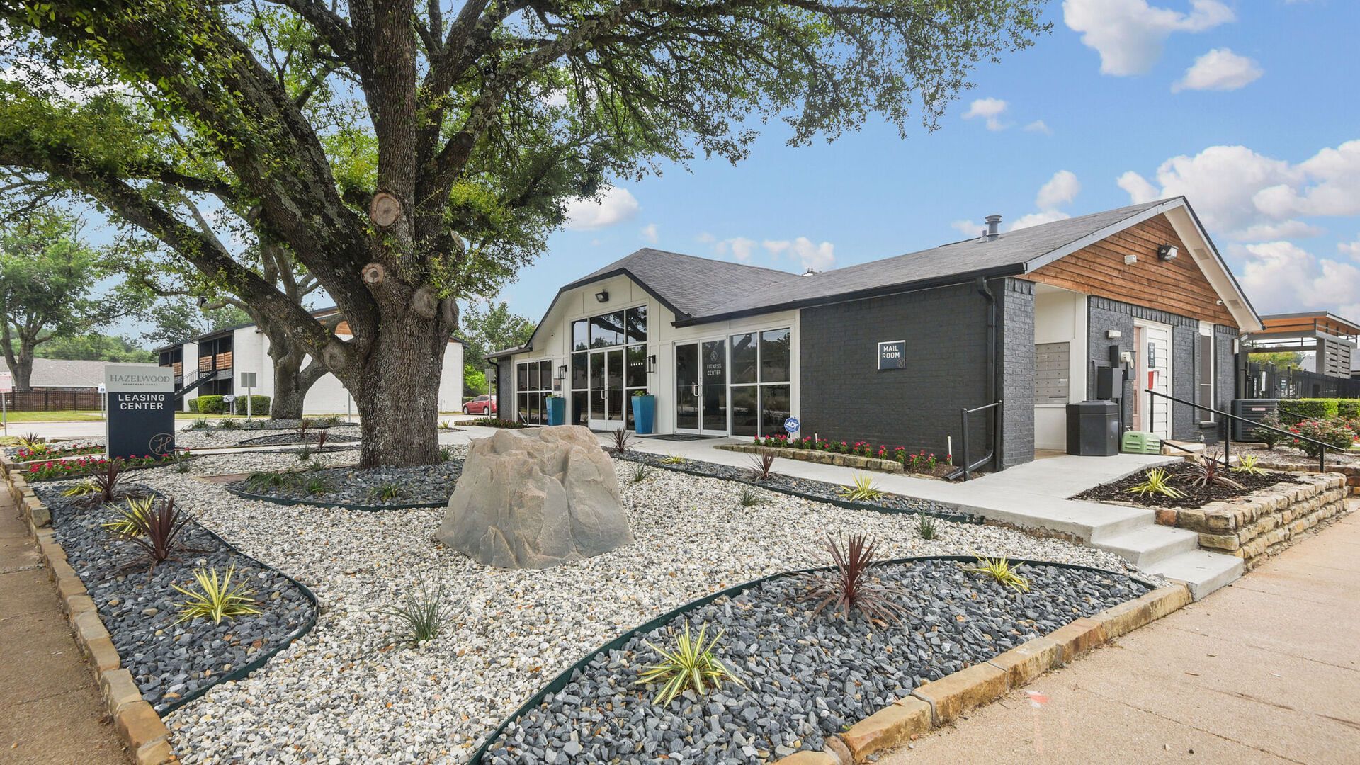Modern building with stone landscaping, large tree, and clear glass windows.
