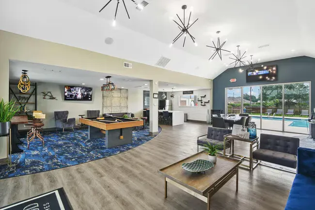 Lounge area with pool table, seating, and large windows overlooking a pool. Modern decor with blue and gray accents.
