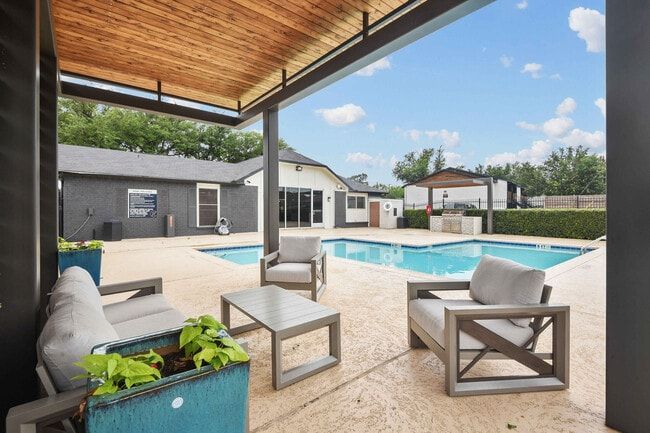 Outdoor patio with pool and seating area. Gray furniture, blue pool, wooden ceiling.