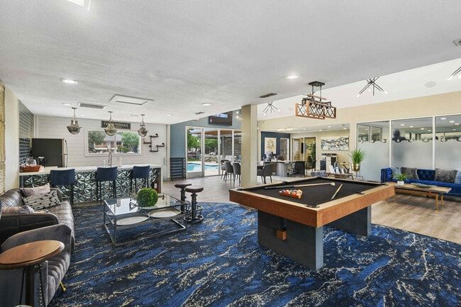 A well-lit recreation room with a pool table, bar, seating, and a view of a pool.