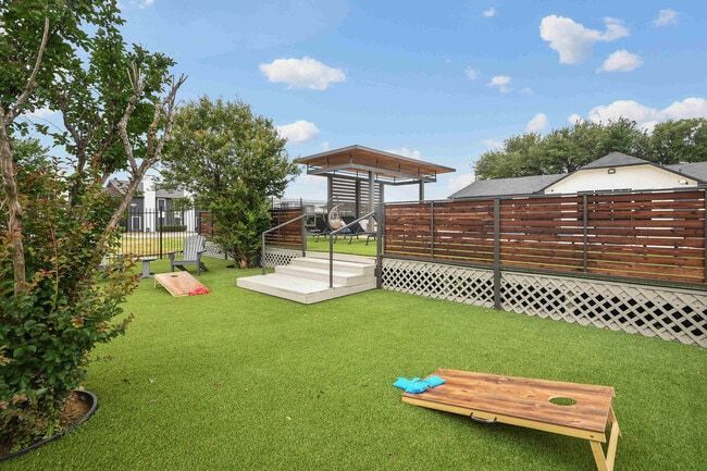Green turf backyard with cornhole, gazebo, and wood fence.