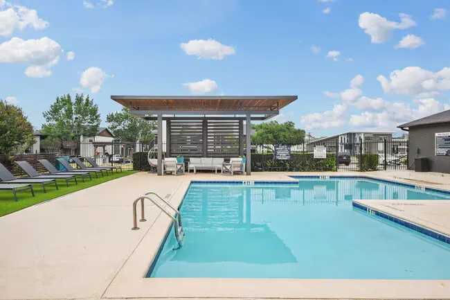 Pool with lounge seating, covered area, and blue sky.