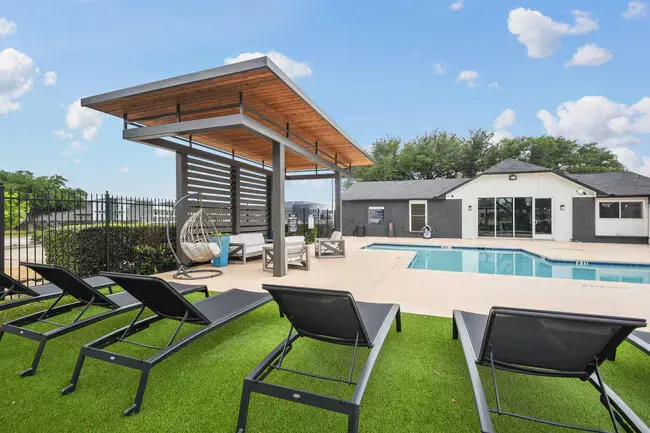 Poolside lounge area with sun loungers on artificial grass, under a shaded cabana.