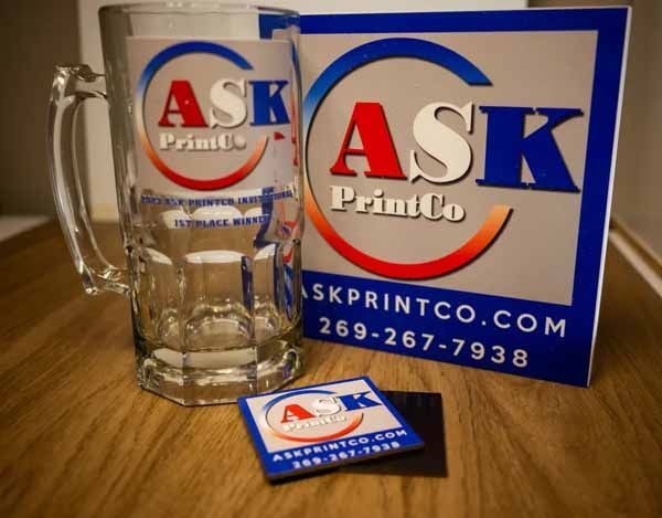 A glass mug sits next to a sign that says ask printco