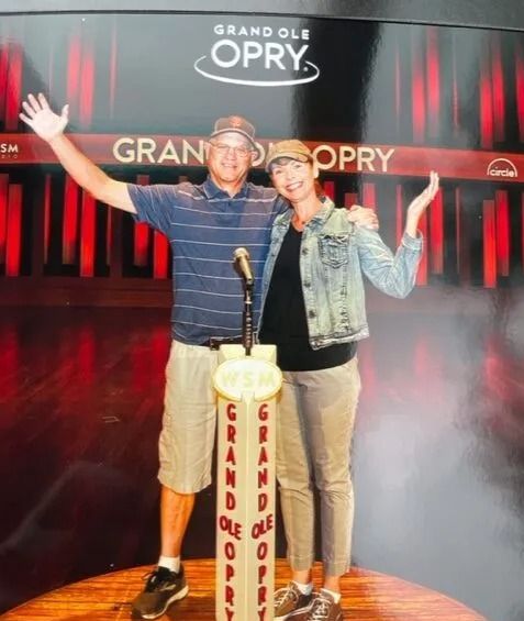 A man and a woman pose in front of a grand ole opry sign