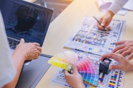 A group of people are sitting at a table with a laptop and a color palette.
