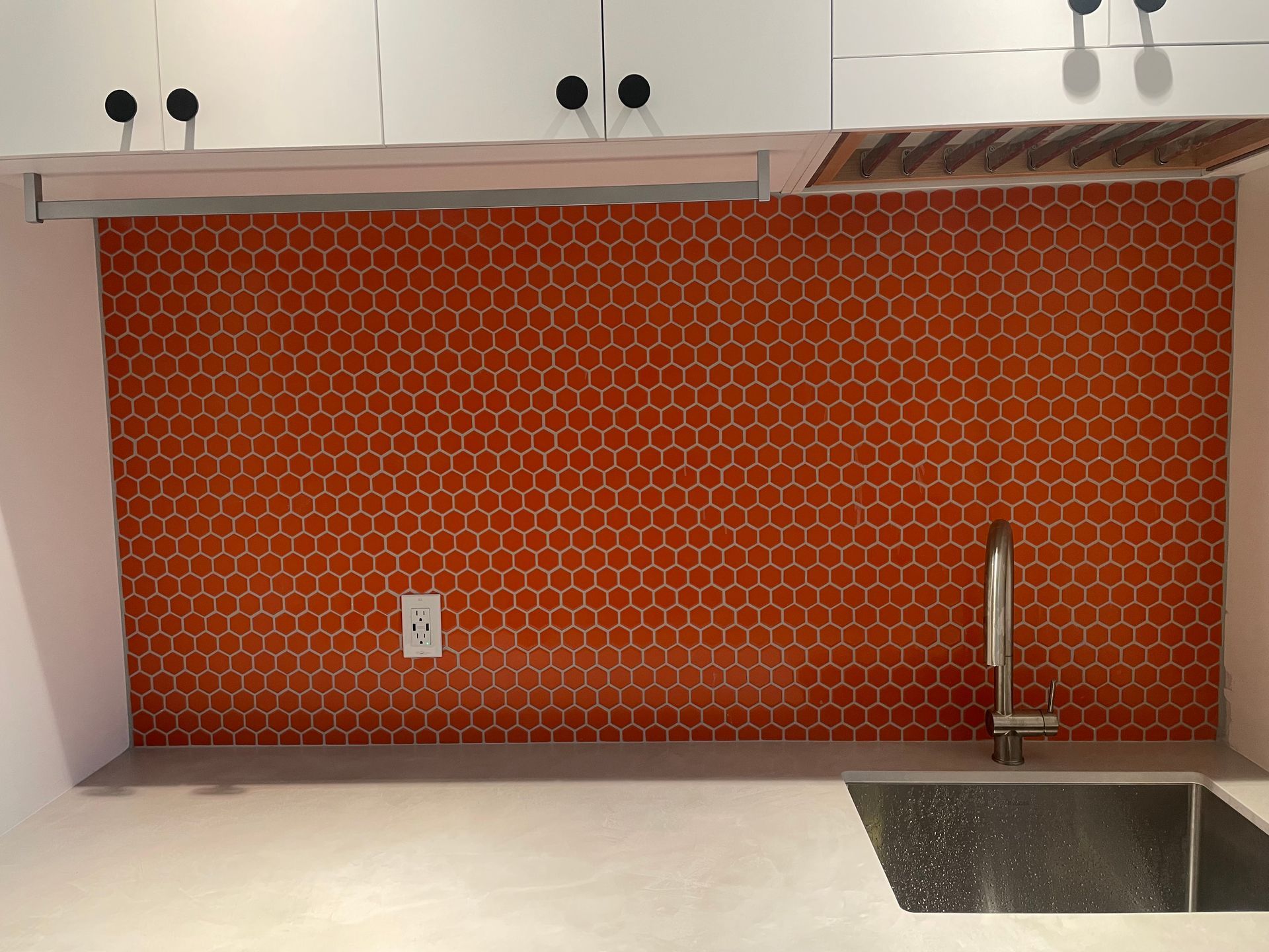 Crédence en carrelage alvéolé orange dans une cuisine, avec robinet, évier et placards blancs.