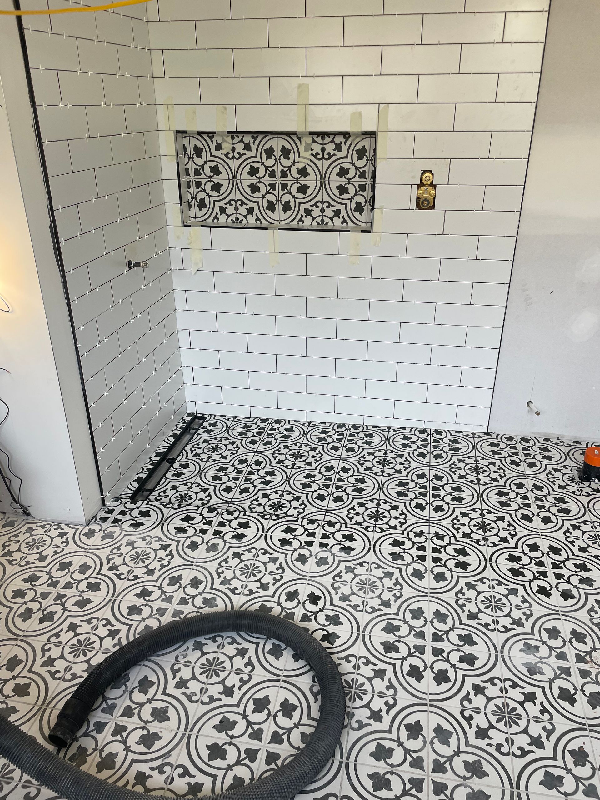 Salle de bains avec carrelage au sol à motifs noirs et blancs, murs carrelés de faïence métro blanche et une frise décorative.