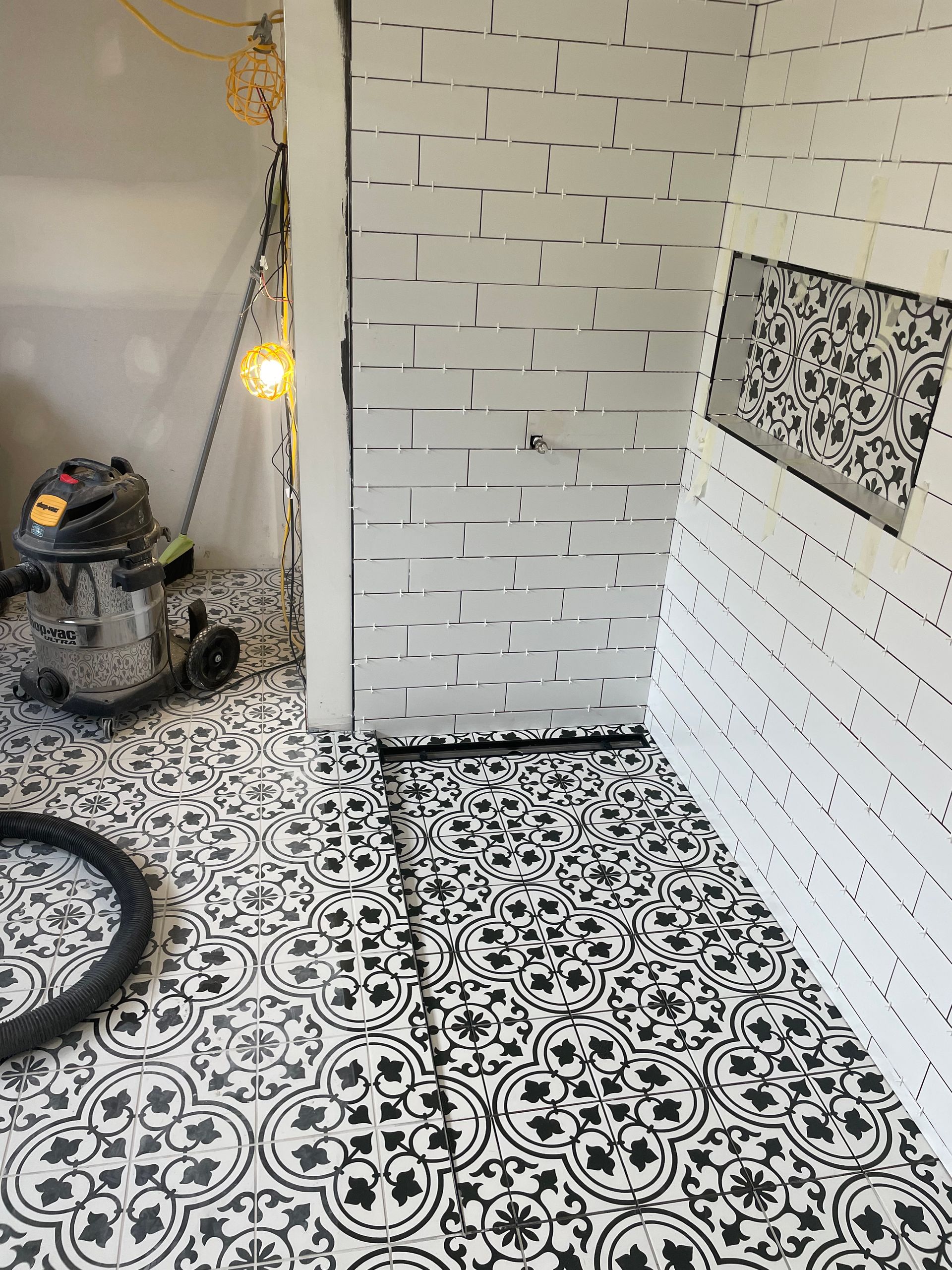 Salle de bains avec carrelage à motifs noirs et blancs, porte blanche et aspirateur.