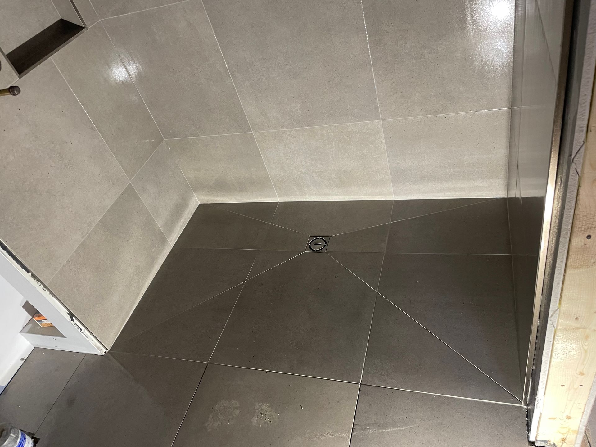 Cabine de douche avec carrelage gris clair et bonde centrale, en construction.