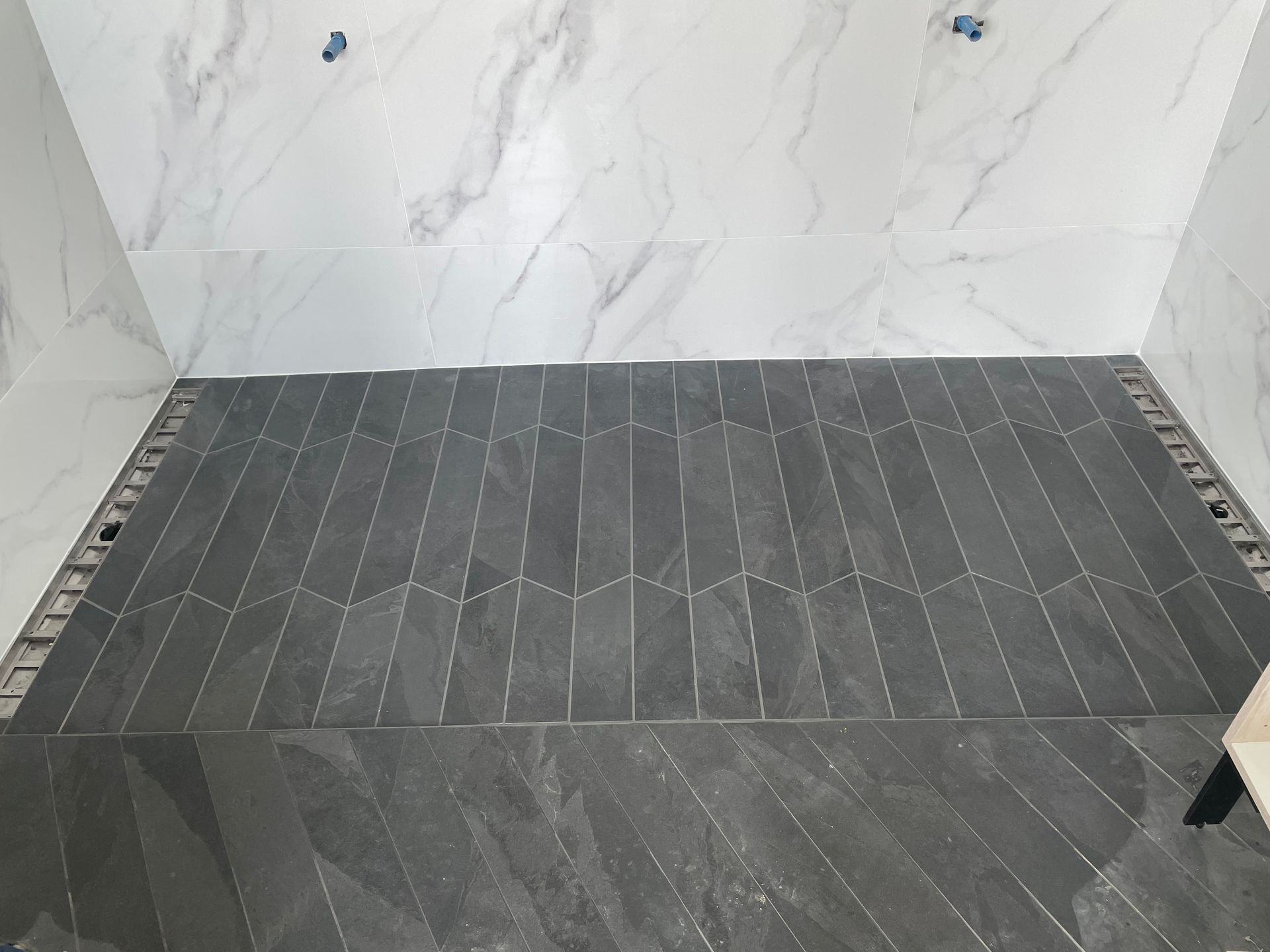 Sol carrelé gris foncé à chevrons, sous un mur en marbre. Chantier.