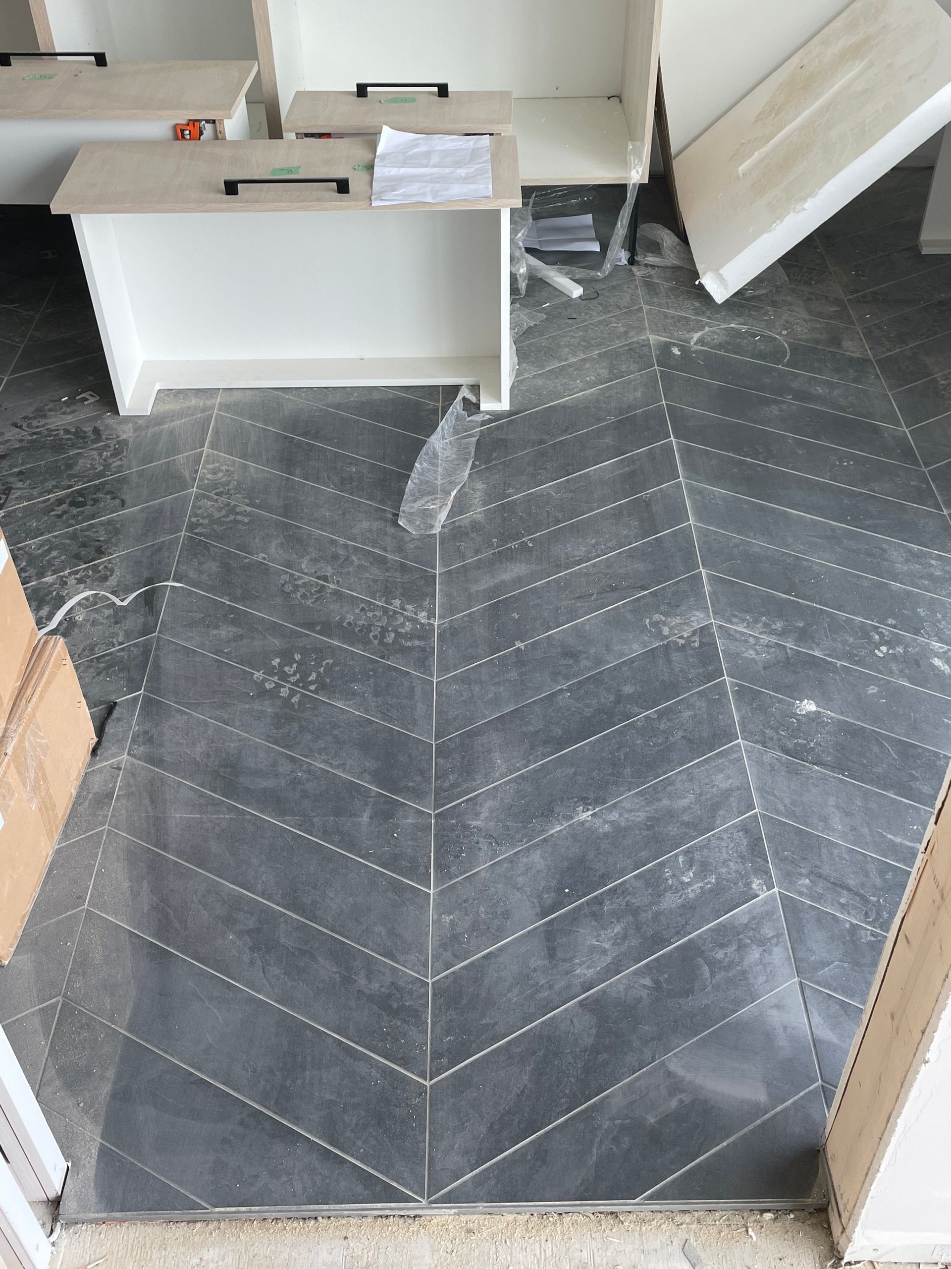 Sol carrelé foncé à chevrons avec des meubles blancs dans un contexte de chantier.