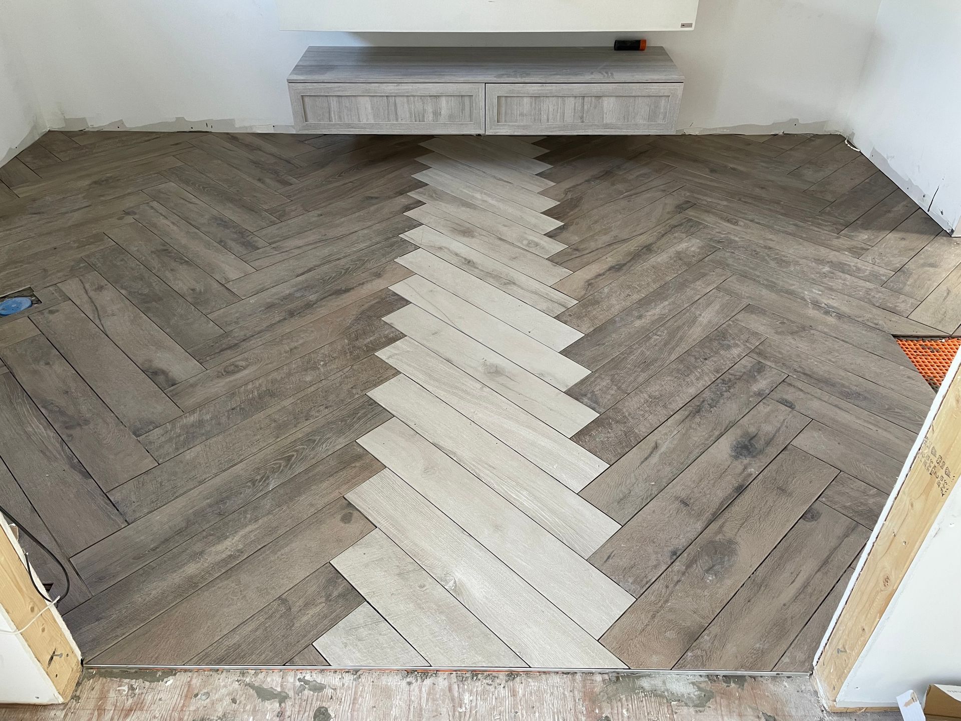 Pose d'un parquet à chevrons avec une bande lumineuse au centre, sous un meuble blanc.