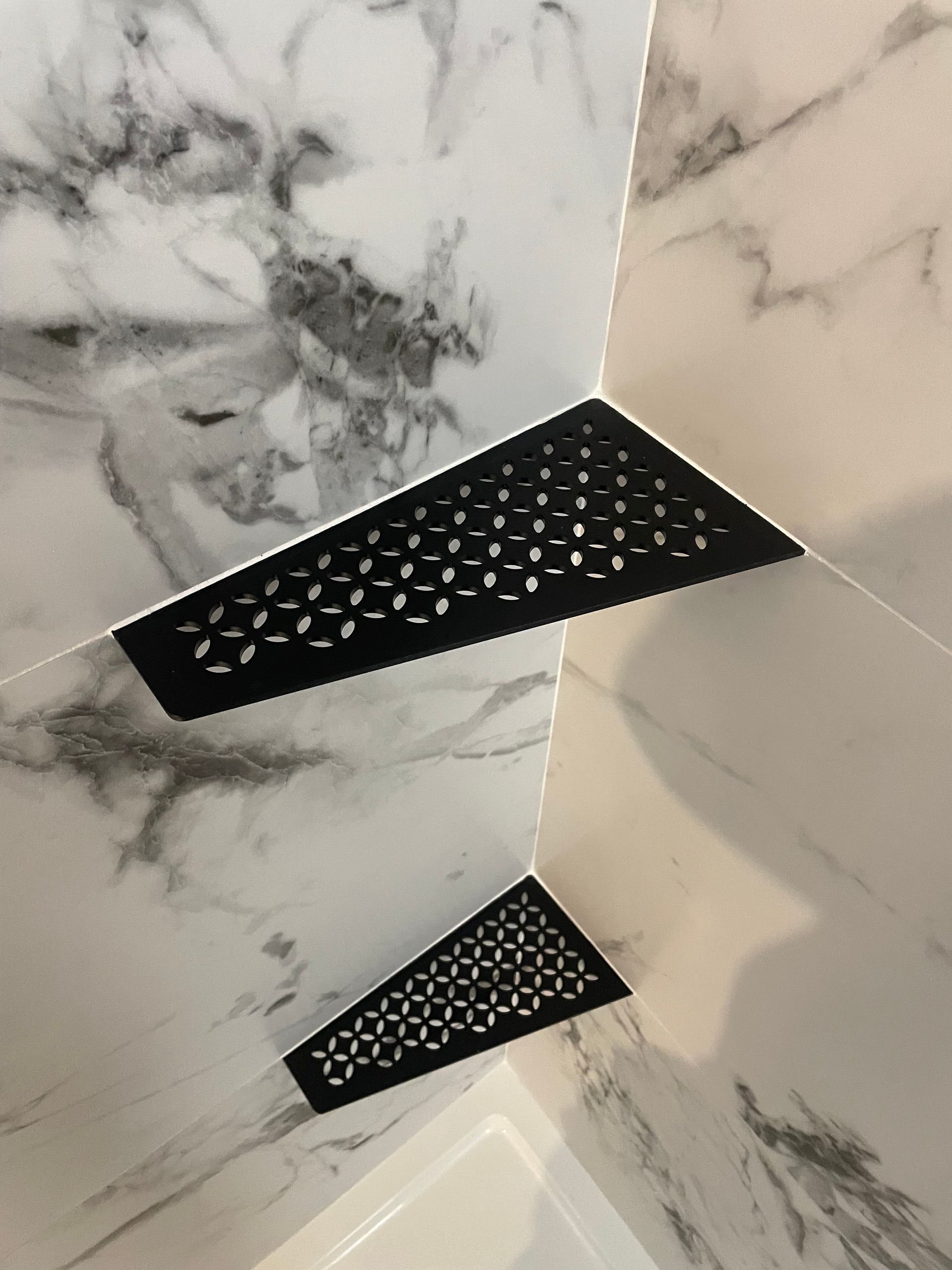 Deux caniveaux de douche décoratifs triangulaires noirs dans un coin carrelé en marbre.