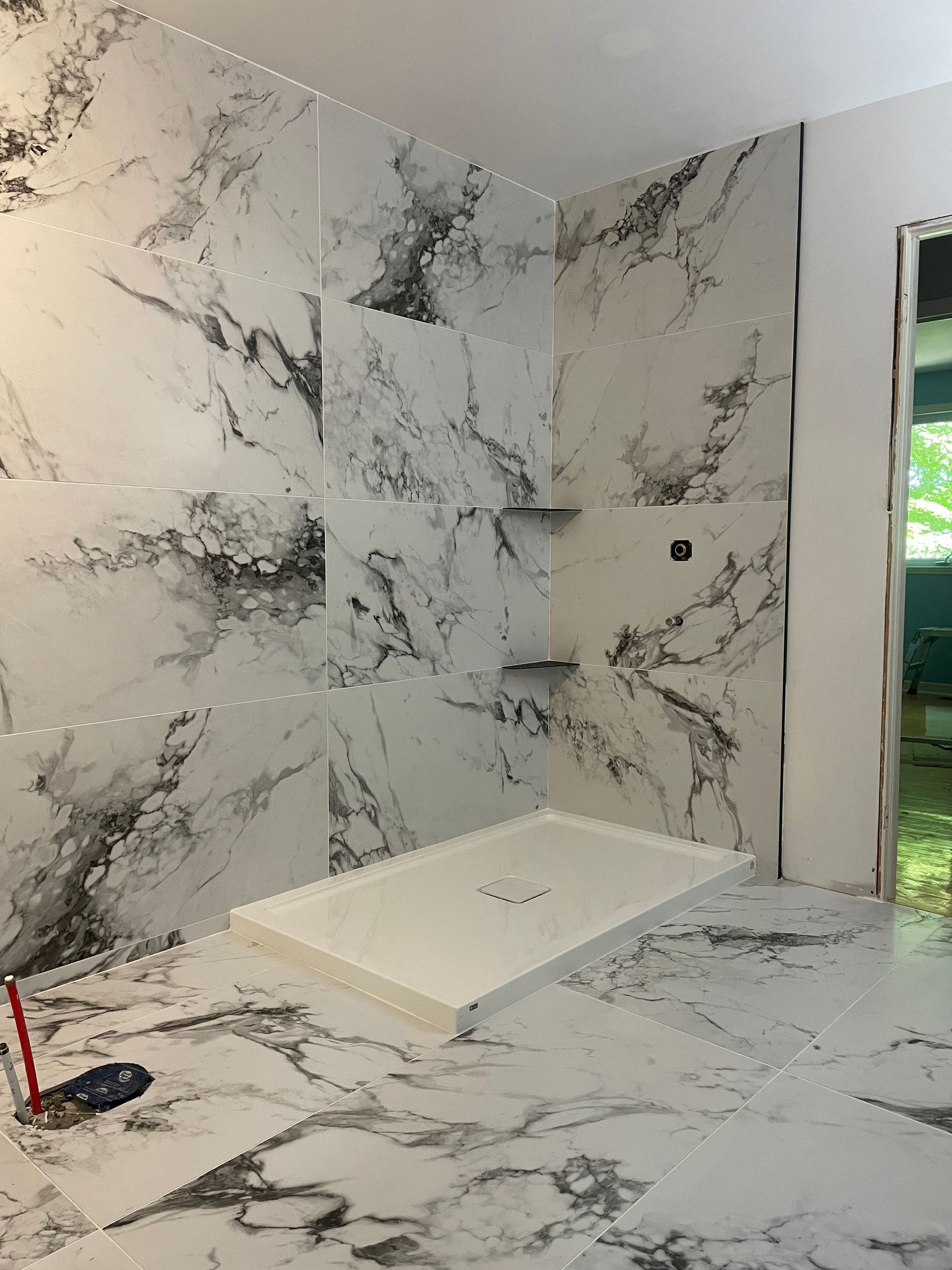 Douche en marbre en cours de réalisation : murs blancs veinés de gris, receveur de douche blanc et deux étagères intégrées.